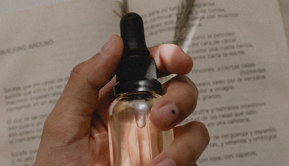 A hand holding a bottle of essential oil next to an open book infused with Hyaluronic Acid.