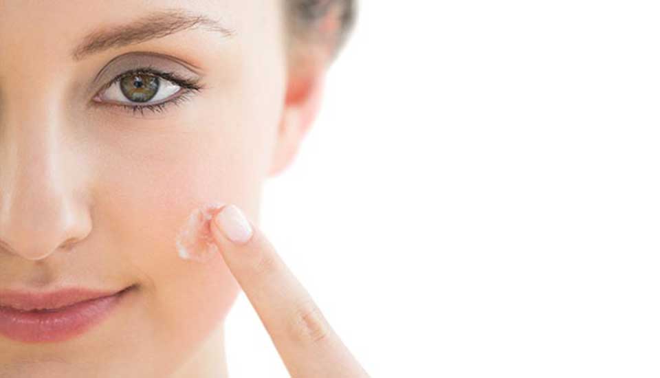 A woman is applying acne cream to her face.